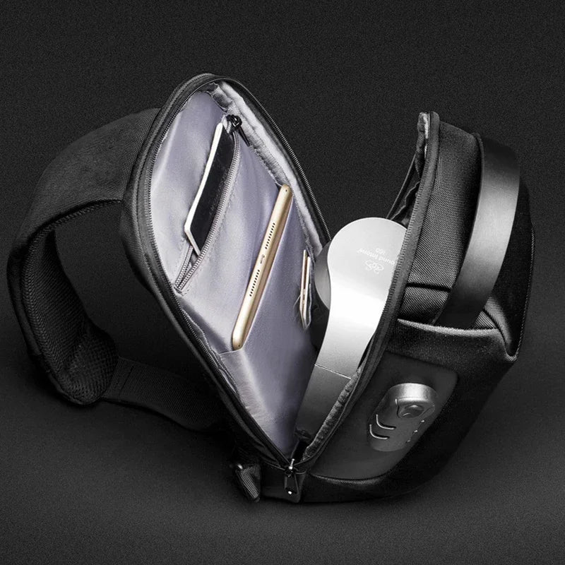 Open black sling bag with organized compartments holding a phone, tablet, and headphones