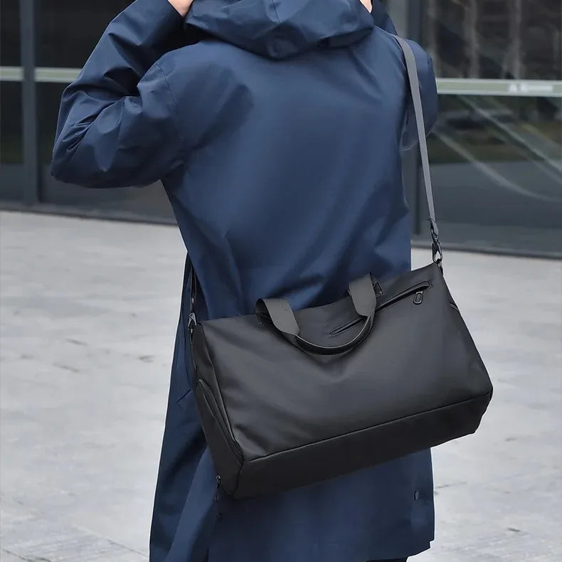 Man in a blue coat carrying a sleek black duffel bag with shoulder strap outdoors