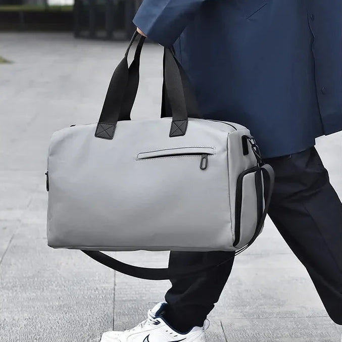 Modern gray duffel bag with black straps carried by person in urban outdoor setting